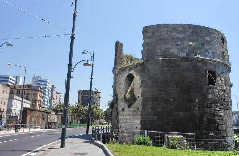 Torri Aragonesi di via Marina Napoli. Antico castello di pietra e torre in rovina nel centro città, con edifici moderni sullo sfondo e percorso pedonale nelle vicinanze.