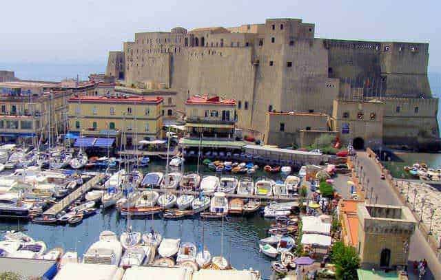 Castello aragonese di Ischia vista dal porto con imbarcazioni e edifici colorati, in un paesaggio mediterraneo ricco di storia e bellezza.
