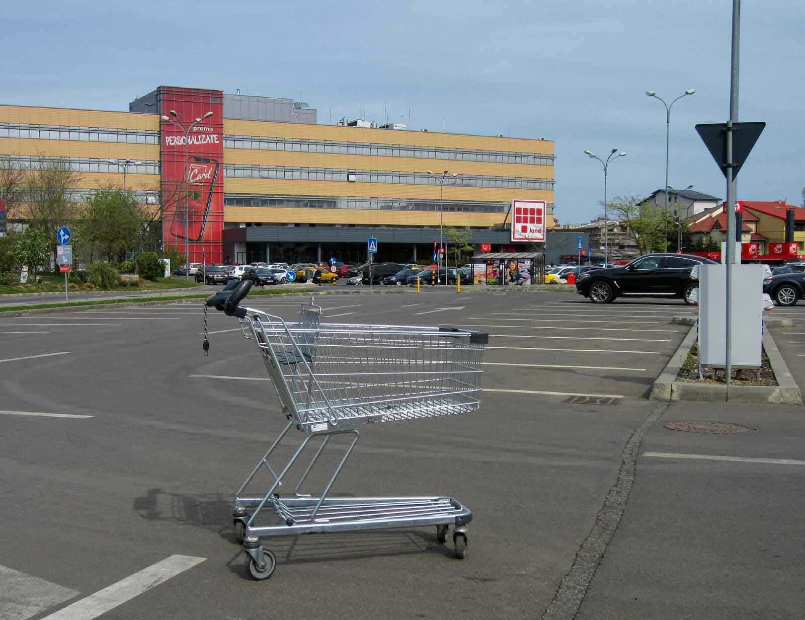 Carrello della spesa in un parcheggio di supermercato con edificio commerciale in background.