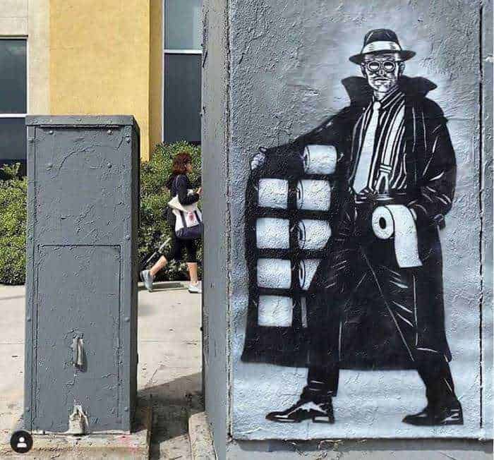 Graffiti di un uomo stilizzato con cappotto lungo e cappello, appoggiato su una parete di città moderna, con studenti e elementi urbani sullo sfondo, in stile street art.