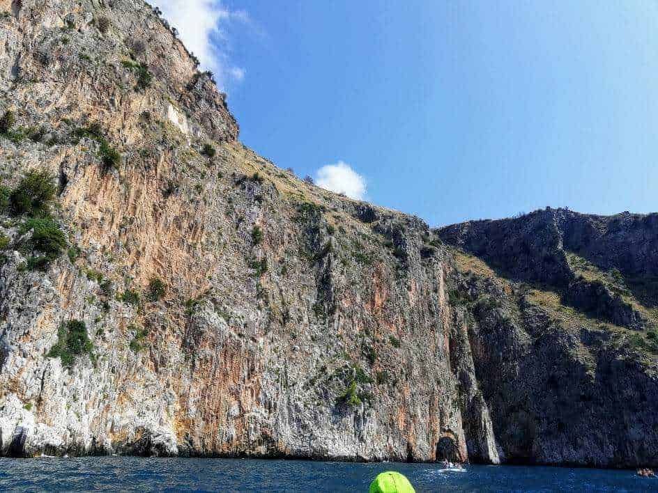 Immagine di una scogliera rocciosa alta e imponente vista dal mare, con acque calme e un cielo sereno, perfetta per escursioni e esplorazioni naturali.