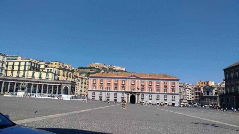 9 Palazzi Neoclassici Napoli e Ville Liberty 2 Palazzi neoclassici e ville liberty a napoli: Tradizionale piazza centrale con edifici storici e vista sul castello in alto a Napoli, Italia. Luogo emblematico ricco di storia e cultura, ideale per passeggiate e scoprire il patrimonio cittadino.