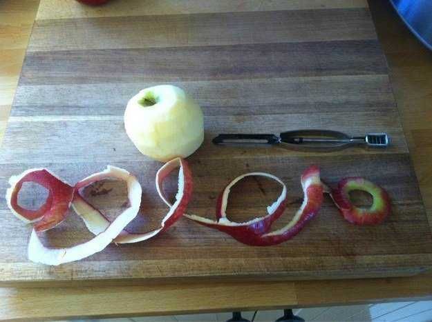 Mela verde e bucce di mela affettate disposte su un tagliere di legno con un pelaverdure, un utensile per pelare e una mela intera pronta per essere sbucciata.