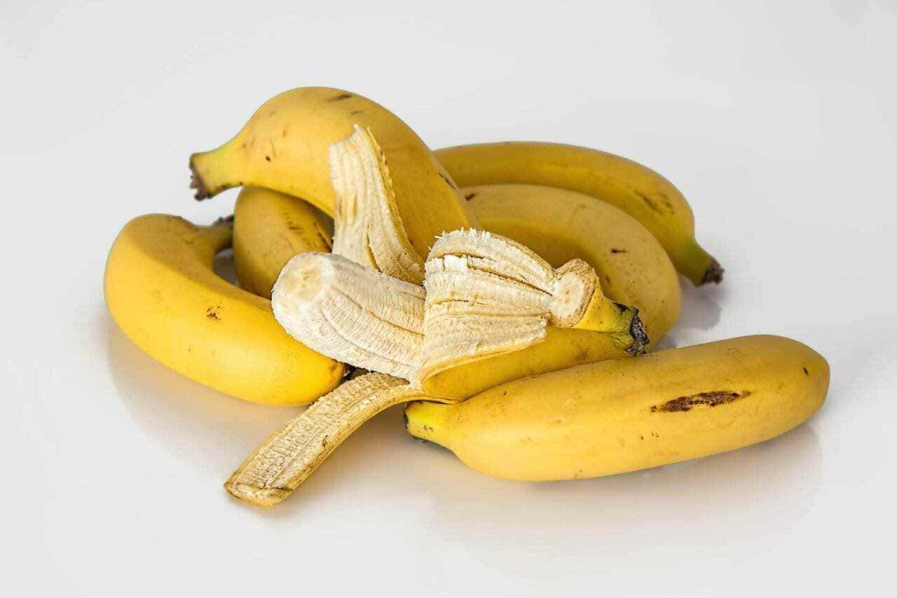 Banane mature e sbuccia di banana fresca su sfondo bianco.