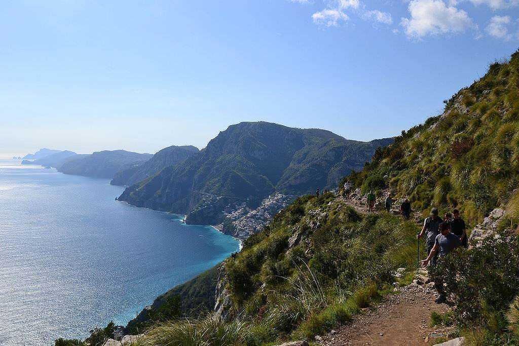 SENTIERO MONTI LATTARI IN CAMPANIA. Vivace spiaggia con barche ricoperte di sabbia, illuminata da lampioni, con case colorate sullo sfondo e scogliera illuminata di notte, scena suggestiva e tranquilla.