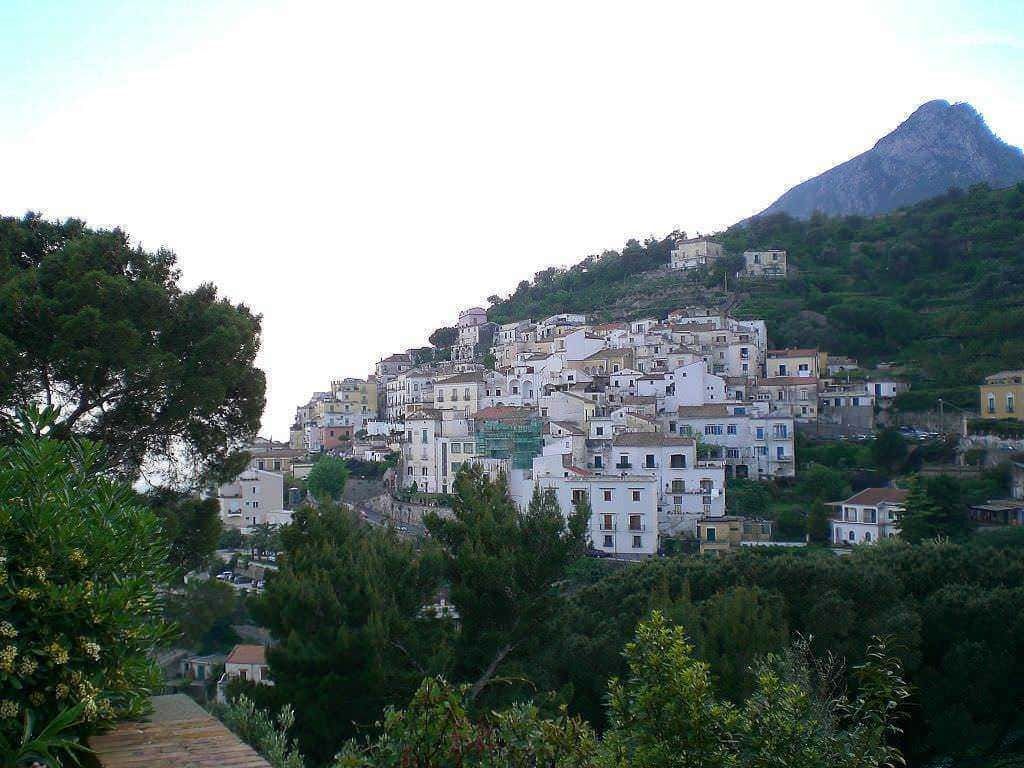 Luminosa veduta di Raito e Albori, caratteristici villaggio sul pendio di una collina con case bianche e strette strade, circondato da verde natura e montagne, scenario perfetto per scoprire le meraviglie della Costiera Amalfitana.