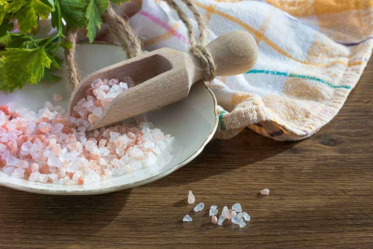 Sale rosa grosso per cucina integrata in sale naturale, ideale per arricchire piatti e alimenti, con cucchiaio di legno su piatto di ceramica, sul tavolo di legno.