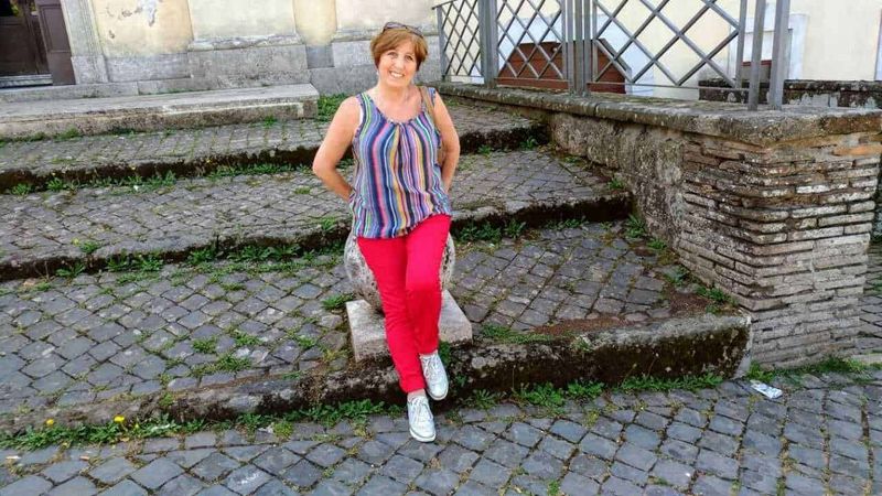 Gold Collagen Active integratore per una vita frenetica e sana 4 Vicina donna seduta su un sedile in pietra su un'area di ciottoli urbani con sfondo di costruzioni storiche.
