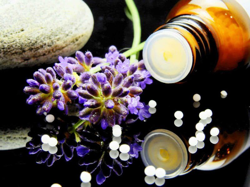 Omeopatia trattamento olistico efficace e diffuso 6 Aromaterapia con olio essenziale di lavanda, pietra levigata e pillole di medicina naturale su sfondo nero.