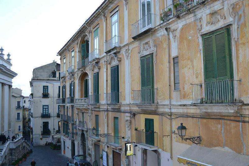 12 Edifici longobardi a Salerno (2026), da Palazzo d'Avossa: stile barocco, coppedè e storia medievale 6 Vecchie facciate di edifici storici a città italiana, edifici con balconi e persiane verdi, immagine di architettura urbana in Italia, edificio con pareti dipinte di giallo, veduta di strada cittadina a Napoli, immagini di architettura italiana, immagine storica di quartiere italiano, strada urbana con edifici storici a Napoli.