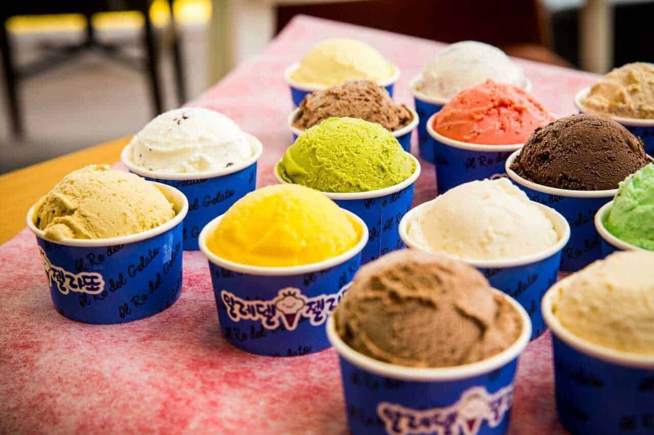 Gelato artigianale in coppe di plastica su tovaglietta rosa, vari gusti di gelato colorati e cremosi, dolcezza estiva, dessert fresco, gelateria italiana, tradizione del gelato.