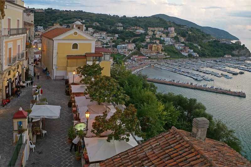 Vicolo caratteristico sul lungomare di Positano con ristoranti, caffè e vista panoramica sulla baia e le barche in mare presa al tramonto.