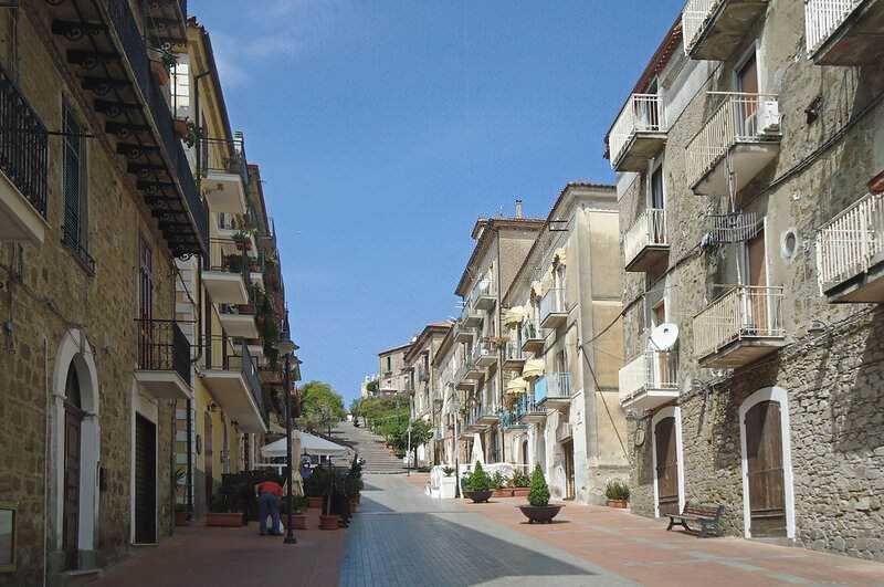Appunti Sul Blog, strada storica con edifici in pietra e balconi fioriti, centro città con negozi e caffetterie, atmosfera mediterranea, trekking urbano, architettura tradizionale italiana, paesaggio pittoresco, cultura locale, turismo in Italia, vie pittoresche.