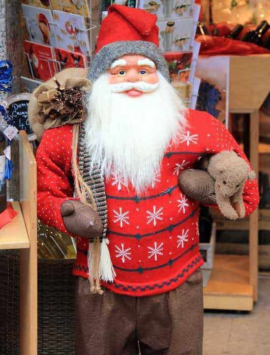 Appesito Babbo Natale in abito natalizio con guanti e cappello rosso, decorato con fiocchi di neve, porta un sacco di doni e un orsacchiotto in negozio di decorazioni natalizie.