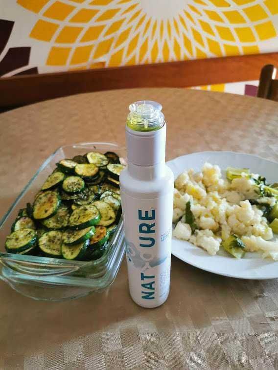 Zucchine grigliate e cavolfiore al vapore con spray nutriente NAT'CURE su tavolo, con sfondo decorativo giallo e marrone, immagini di pietanze salutari e benessere alimentare.