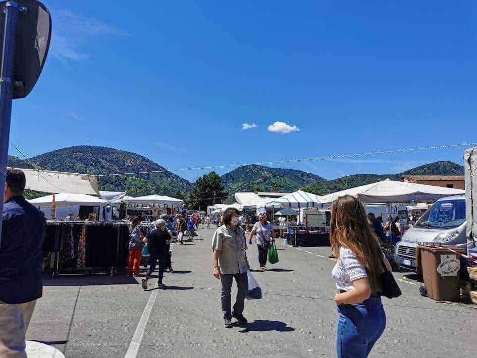 Passeggiataalmercatoallapertoconstand,epeoplecheesplorano ilmercato,montagnedeliberamentiinbackground,clima soleggiato,impossibileresistereallebellezzedellasalassiudice.