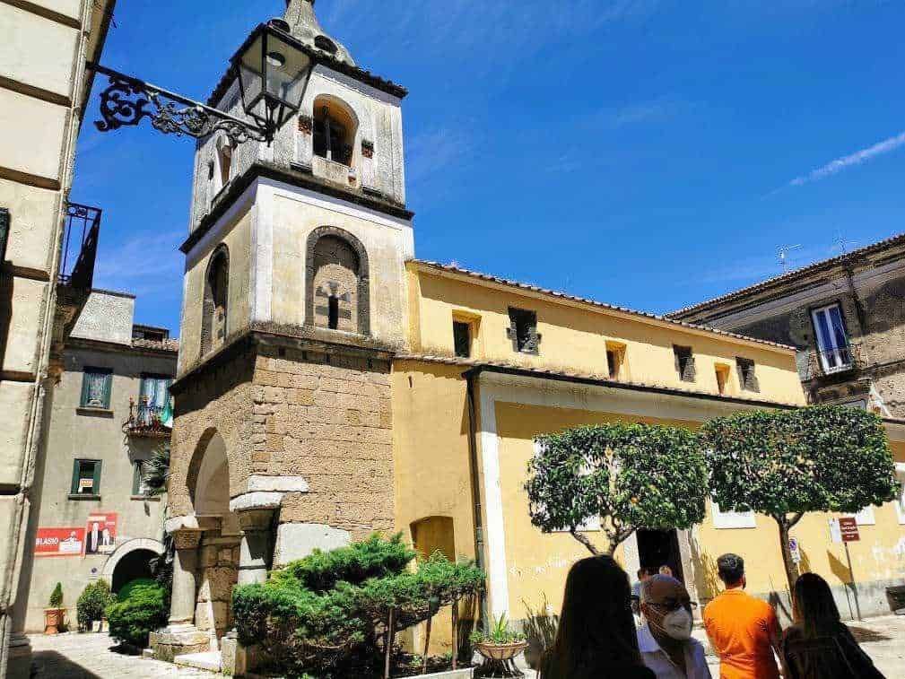 Antico campanile e palazzo storico nel centro di una città italiana, con cielo blu e persone che passeggiano, in stile architettura tradizionale italiana.