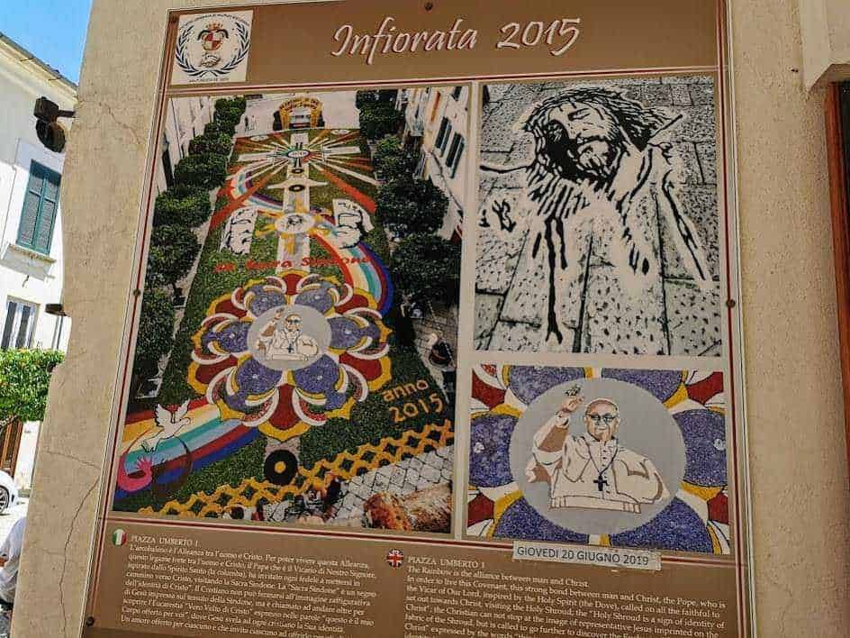 Il-ALT: Dettaglio dettagliato di una decorazione floreale di grandezza naturale con tema religioso, realizzata nel centro di una città italiana, con colori vivaci e simboli religiosi.