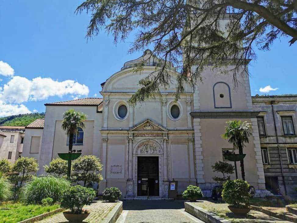 Iconica chiesa storica con architettura barocca, circondata da un giardino ben curato e alberi secolari, in un affascinante paesaggio di montagna sulle colline italiane.