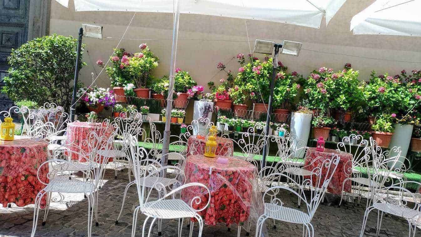 Balcone con tavoli in ferro battuto e fiori colorati, spazio esterno per relax e socializzazione in un ambiente estivo e accogliente.