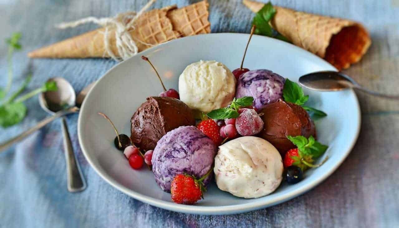 Gelato artigianale con gusti alla frutta, cioccolato e vaniglia servito in una ciotola bianca, decorato con frutti di bosco e foglie di menta. Scopri le migliori ricette di gelato fai-da-te su Appunti Sul Blog.