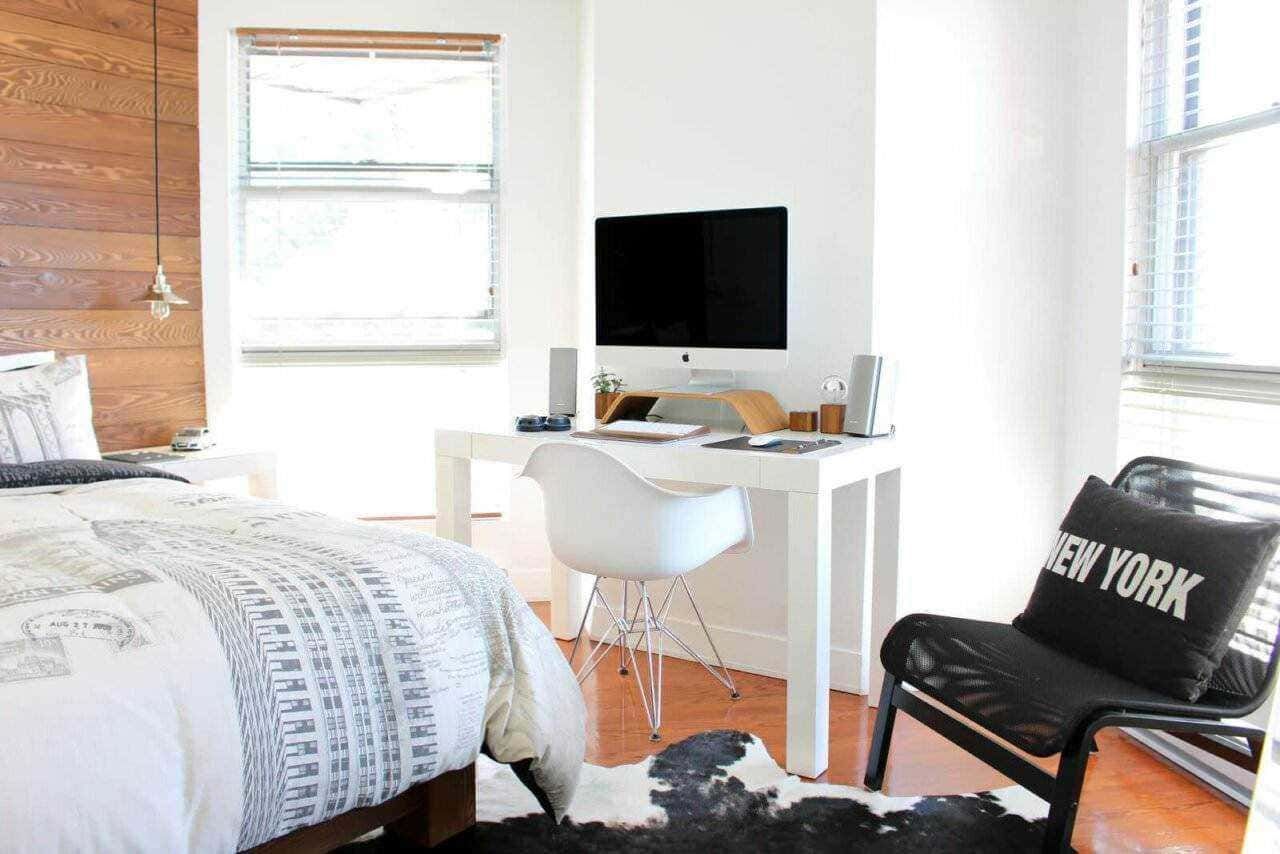 Finestra luminosa in camera da letto con arredo minimalista, scrivania moderna con computer e sedia bianca, dettagli di decorazione contemporanea, ambiente accogliente e ben illuminato.