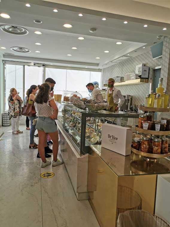 Gelato artigianale in una gelateria moderna con clienti in fila, ambiente luminoso, esposizione di gusti diversi, servizio attento, atmosfera accogliente, ricercata e di tendenza, in centro città, preferibile a fine pasto o pausa dolce, foto di alta qualità, dettagli accurati, arredamento minimale, cliente che sceglie il gelato, staff professionale, ambiente pulito, stile contemporaneo, decorazioni eleganti, atmosfera dinamica, moda lifestyle, gelatieri in divisa, prodotti di alta qualità, interior design elegante, esperienza di gusto, consumatori soddisfatti, stagione estiva, autenticità, innovazione gelato, cultura del gelato artigianale.