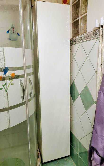 Mobili da bagno sospesi per piccoli bagni moderni 2 Armadio bianco alto in ambiente bagno con pareti rivestite di piastrelle verdi e beige, elegante e funzionale per la conservazione di vestiti o accessori.