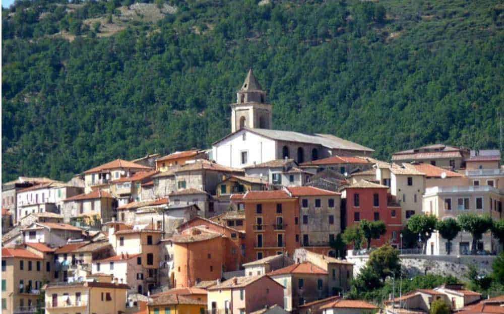 Vicoli colorati di un borgo italiano con chiesa storica in collina verdeggiante.