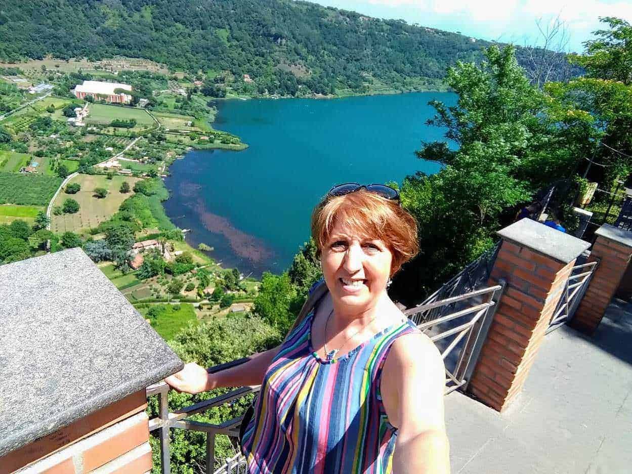Lago suggestivo vista dall'alto con donna che scatta selfie sul balcone in estate, paesaggio naturale e verdeggiante.