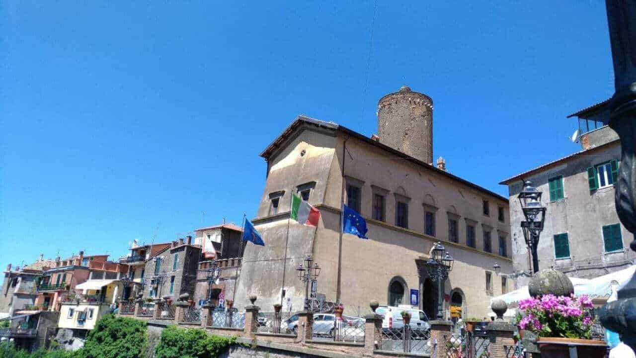 Ville storiche italiane con bandiere e architettura tipica, sotto un cielo azzurro.