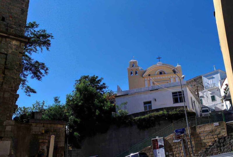 6 Comuni isola Ischia, cosa fare in 3 giorni 12 Villa storica su collina con chiesa barocca sotto un cielo azzurro, contorni di case bianche e verde foliage, atmosfera mediterranea, in un paesaggio urbano di Napoli, Italia.