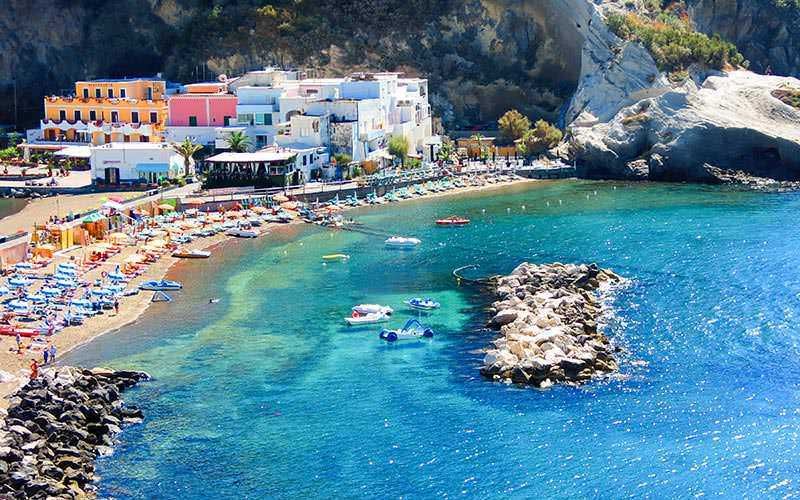 Colorato villaggio balneare sulla costa italiana con spiaggia affollata, onde cristalline e case colorate, ideale per vacanze estive e relax sul mare.