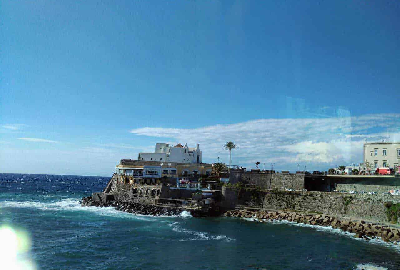 Spiaggia di Sliema con vista sul mare e edifici storici, cielo azzurro e onde che si infrangono sulla costa.