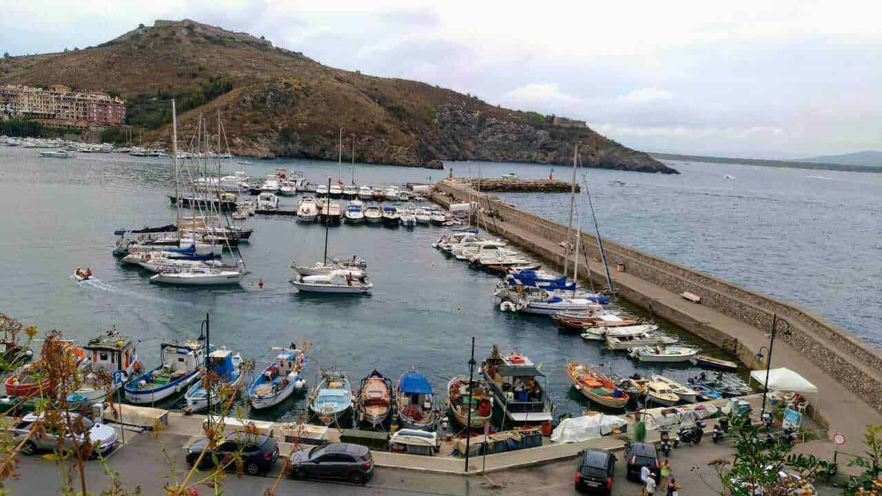 Barca, porto turistico e paesaggio costiero in Italia, con vista sul mare, imbarcazioni, promontorio e cielo nuvoloso, perfetto per articoli di blog su destinazioni di viaggio.