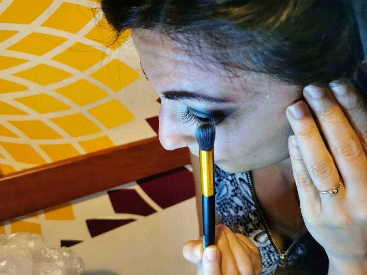 Pennello da trucco in azione mentre una donna applica l'ombretto sugli occhi, con attenzione ai dettagli e alla precisione. L'immagine evidenzia tecniche di make-up professionale e bellezza femminile.