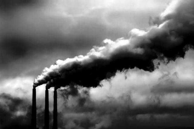 Fili di fumo denso e scuro che escono da una fabbrica industriale, simbolo dell'inquinamento atmosferico e dei cambiamenti climatici. Problemi ambientali legati alle emissioni di carbonio e alla cattiva gestione delle risorse naturali.