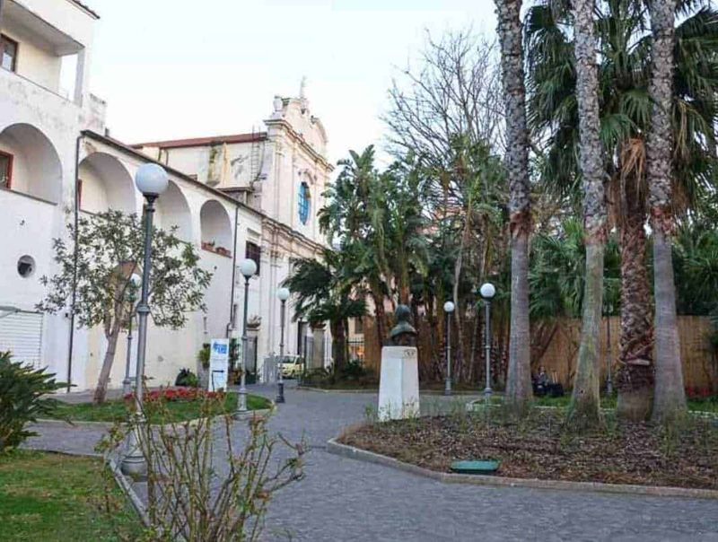 6 Edifici religiosi a Sorrento. Quali sono? 7 Vecchio edificio storico con giardino urbano e palme, atmosfera tranquilla e rilassante, ideale per passeggiate e relax, decorazioni eleganti con lampioni e statue, ambientazione suggestiva, perfetta per appunti sul blog di viaggi o cultura italiana.