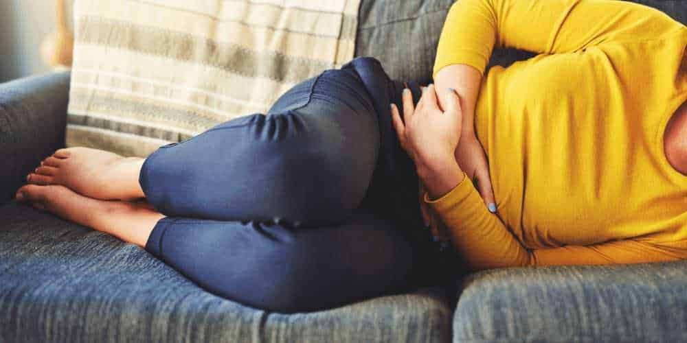 Dolore addominale e crampi in un giovane donna sdraiata sul divano, dolorante, in un ambiente domestico.