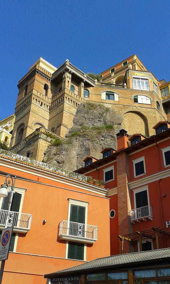 Vista di edifici colorati e storici a Positano, Costiera Amalfitana, con case color arancione e dettagli architettonici caratteristici, sotto un cielo blu Limpido, perfetta per foto di viaggio e turismo in Italia.