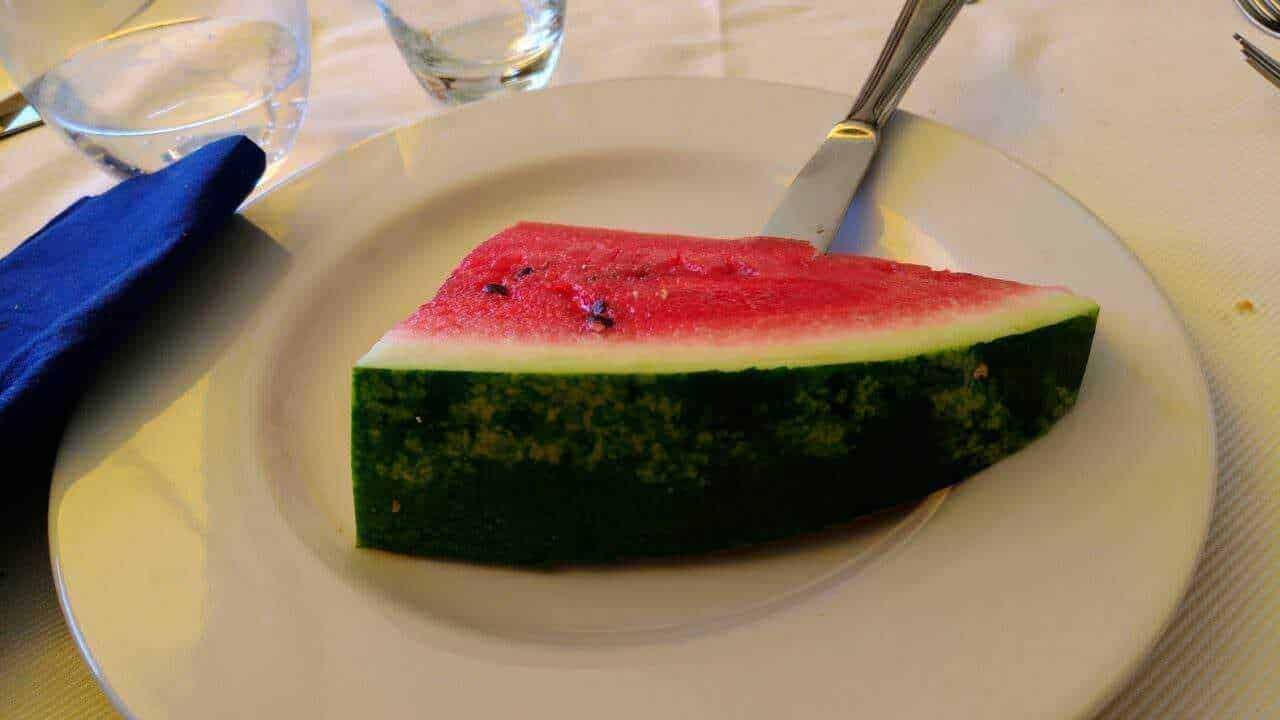 Genera un’immagine di una fetta di anguria fresca su un piatto elegante, perfetta per blog di cibo, ricette estive e frutta fresca. Ideale per articoli su alimentazione sana e rinfrescante.