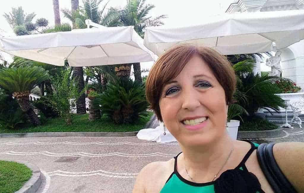 Fotocamera di una donna con occhiali da sole sulla spiaggia, mare e pedane con sedie e ombrelloni in sfondo, estate e vacanze al mare, ritratto di donna sorridente in abbigliamento estivo, viaggio e relax al sole.