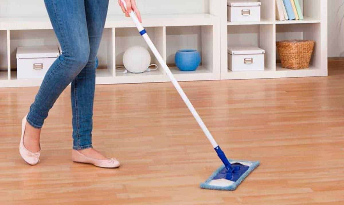 Pulizia pavimenti con mocio in casa, donna che raccoglie lo sporco, ambiente domestico pulito e ordinato, rappresentazione di cura e manutenzione degli spazi abitativi.