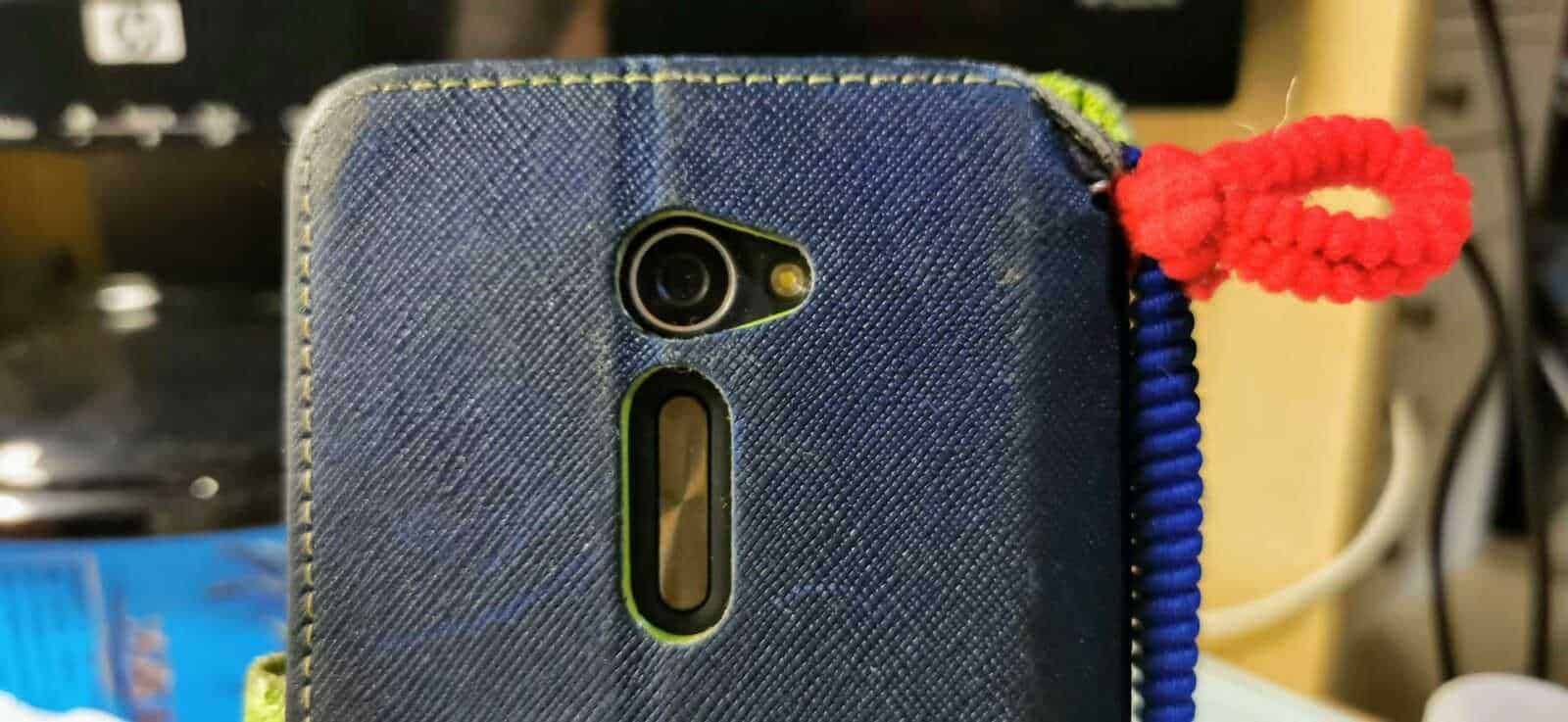 Smartphone con cover in tessuto blu e decorazione a fiore rosso, dettaglio di uno smartphone utilizzato quotidianamente, con focus sulla camera e il design del dispositivo.