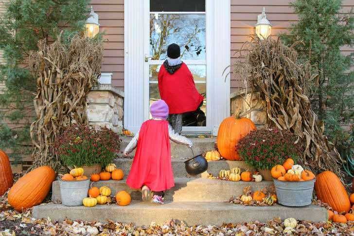 Zucche di Halloween e decorazioni autunnali sulla porta d'ingresso, con bambini in costumi che si preparano per festeggiare Halloween, ambiente festoso e accogliente.