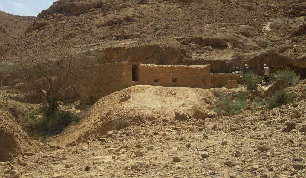 Via dell'Incenso: Antiche rovine di un insediamento desertico in muratura, circondato da rocce e vegetazione secca, con due persone che esplorano l'area.