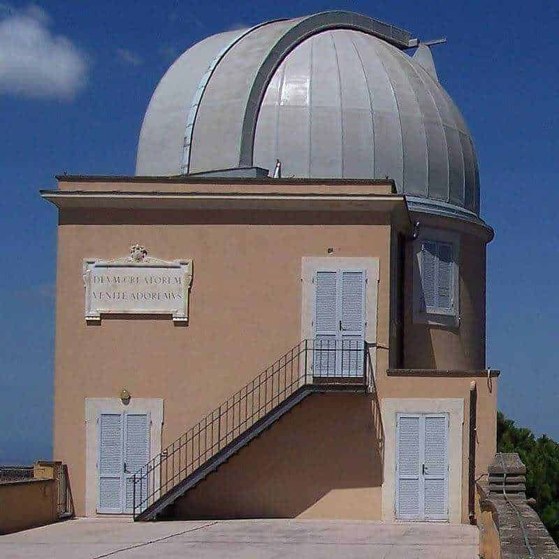 Osservatorio astronomico con cupola in metallo, edificio in stile classico con scalinata esterna, luminosa facciata beige e dettagli in bianco, cielo blu sullo sfondo, sito di appunti e blog di approfondimenti scientifici.
