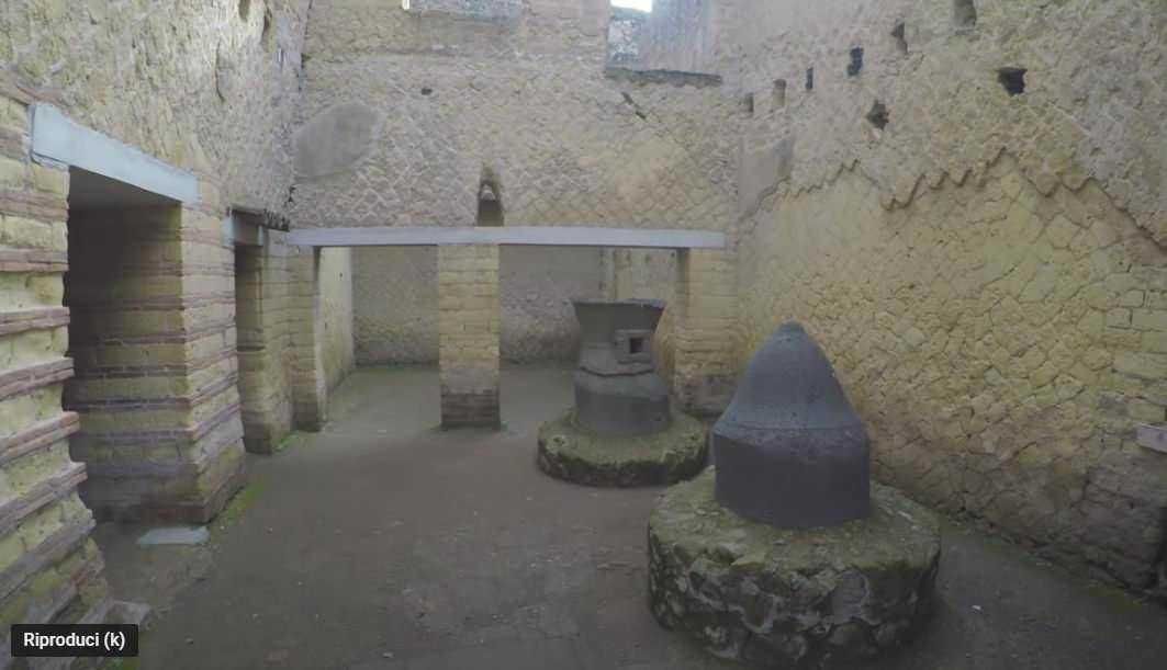 Coperchio in vetro a protezione della porta d'ingresso di un edificio storico, dettagli architettonici in pietra, ambiente urbano, donna con capelli ricci e occhiali da sole.