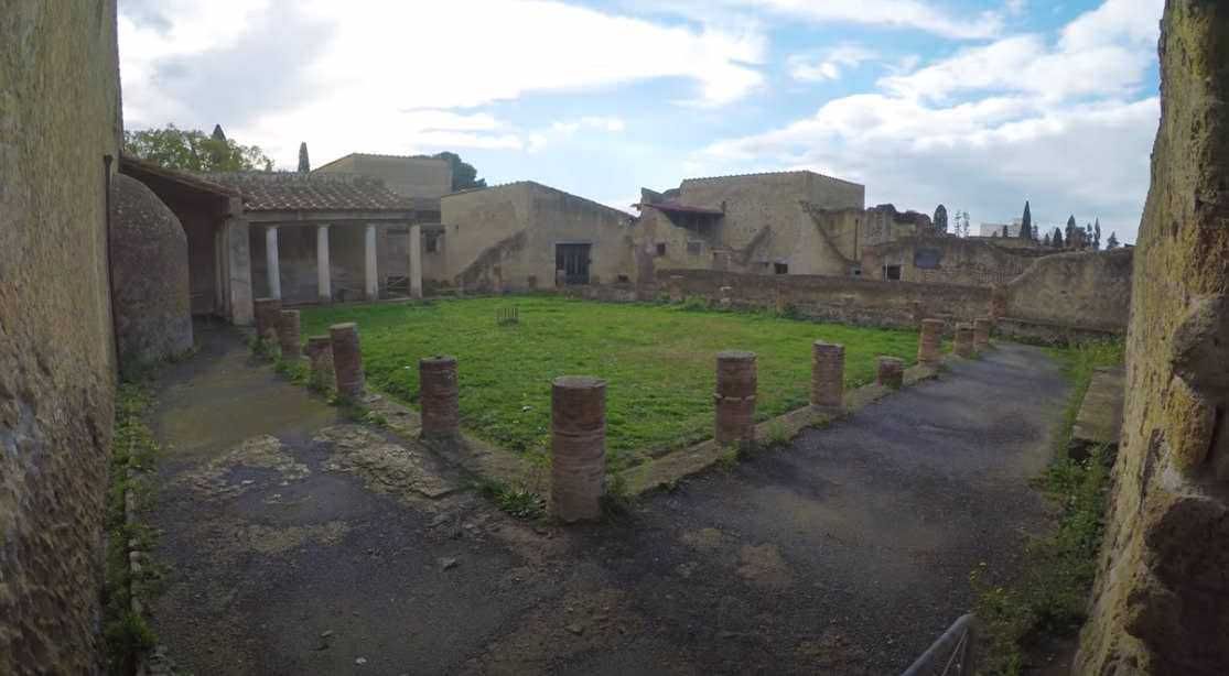 Ancient Roman archaeological site with ruins, columns, and a central grassy area, showcasing historical remains and architecture in Italy.