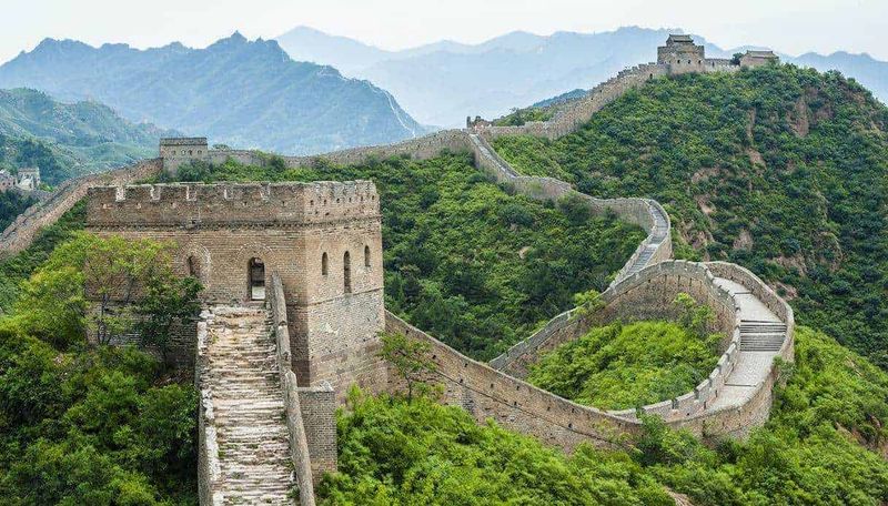 Grande Muraglia cinese storia e curiosità sito Unesco 3 Antica sezione della Grande Muraglia Cinese che si snoda attraverso verdi colline montane. Vista panoramica del patrimonio storico cinese immerso nella natura. Panorama delle mura della Grande Muraglia con viste sulle montagne sullo sfondo.